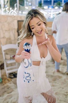 a woman standing on top of a sandy beach holding an object in her hand and smiling at the camera