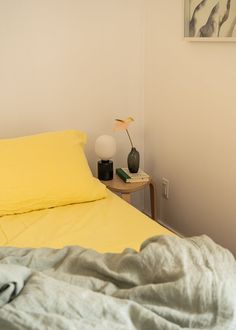 a bed with yellow sheets and two vases on the end table next to it