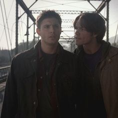 two young men standing next to each other in front of a train track and power lines