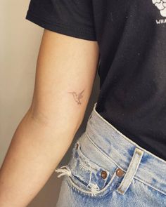 a person with a small bird tattoo on their left arm and the other arm behind her