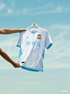 a person holding up a soccer jersey in front of a blue sky with white clouds