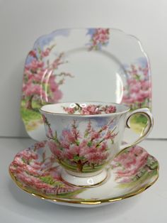 a tea cup and saucer with pink flowers on the side, sitting next to each other