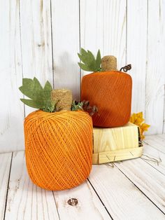 two yarn pumpkins sitting next to each other on top of a wooden board with leaves