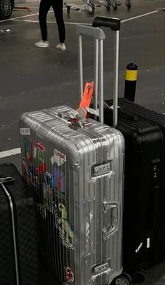 two pieces of luggage sitting on the ground in a parking lot with people walking by