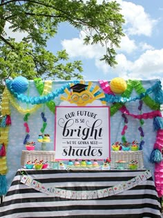 a bright and colorful graduation party is set up under a tree with balloons, tassels, and streamers