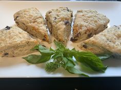 four scones are arranged on a white plate with green leafy garnish