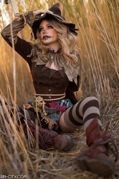 a woman dressed as a scarecrow sitting in the grass