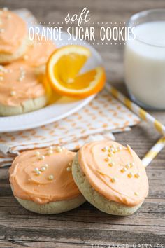 orange sugar cookies with frosting and sprinkles on a plate next to a glass of milk