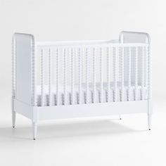 a baby crib with white bedding on the bottom and sides, in front of a plain background