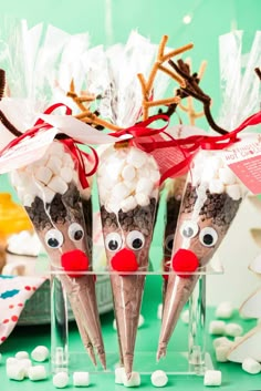 three cones with reindeer noses and marshmallows in them on a green table