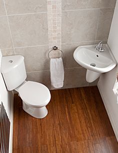 a small bathroom with wood flooring and white fixtures, including a toilet and sink