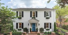 a white house with black shutters on the front and blue door, surrounded by trees