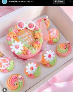 cupcakes decorated with flowers and peace signs are on display in a pink box