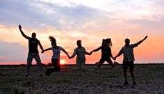 a group of people jumping in the air at sunset