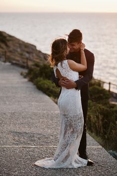 a bride and groom hugging on the beach at sunset with the ocean in the background