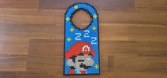 a bottle opener made out of perler beads on a wooden floor with a mario mouse design