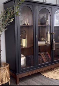 a black china cabinet with glass doors on the front and shelves above it, next to a potted plant