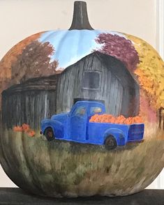 a painted pumpkin with a blue truck in the front and an old barn in the back