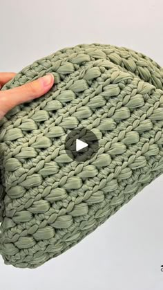 a hand holding a green knitted bag with a hole in the middle and a button at the bottom