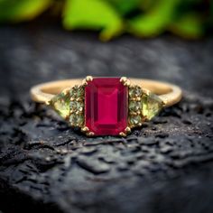 a close up of a ring with a red stone and two green stones on it