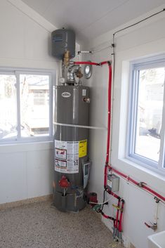 a water heater in the corner of a room next to a window and pipes