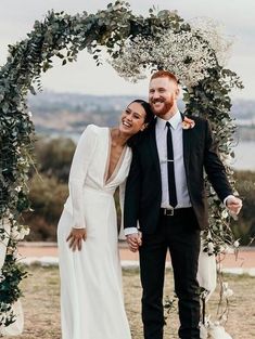 a newly married couple standing under an arch with greenery and white flowers on it