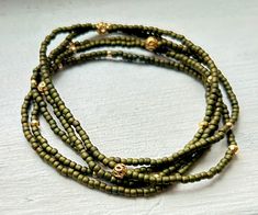 Made with olive green Czech glass seed beads and complementary latticed gold metallic seed beads, our wrap bracelets are designed to add a touch of bohemian flair to any outfit. Handcrafted with strong elastic cording, these stretchy bracelets effortlessly wrap around your wrist five times or around your neck two times as a choker-style necklace, providing a comfortable, lightweight, durable fit for all-day wear and active outdoor play.Each bracelet features a beautiful combination of seed beads Gold Bohemian Wrap Bracelet With Faceted Beads, Bohemian Gold Wrap Bracelet With Tiny Beads, Bohemian Green Beaded Bracelets With Gold Beads, Gold Multi-strand Spiritual Beaded Bracelets, Spiritual Gold Multi-strand Beaded Bracelets, Gold Hand Wrapped Beads For Festival, Gold Bohemian Wrap Bracelet With Spacer Beads, Gold Hand-strung Wrap Bracelet For Festivals, Gold Bracelets With Spacer Beads For Festival