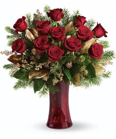 a vase filled with red roses and greenery on a white background for the holiday season