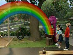 children are standing in front of a tree with a rainbow painted on it and an elephant statue