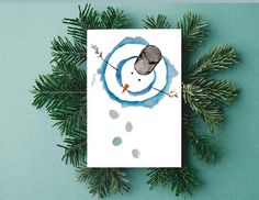 a christmas card with a snowman drawn on it and pine branches next to it