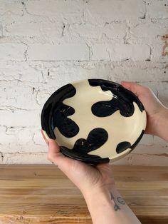 a hand holding a black and white bowl on top of a wooden table