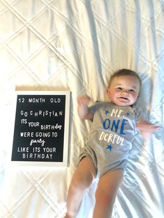 a baby laying on top of a bed next to a sign that says 12 month old