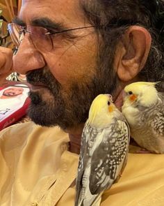 a man is holding two birds in his hand and looking at the camera while another bird sits next to him