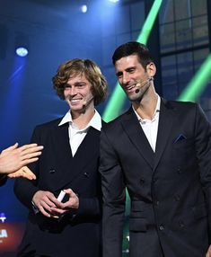 two men standing next to each other in front of green and blue lights on stage