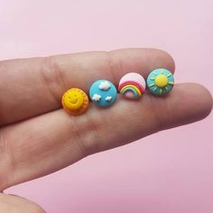 a person's hand holding three small toy doughnuts in the shape of sun, cloud, and rainbow