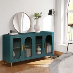 a room with a bed, mirror and blue cabinet in front of a large window