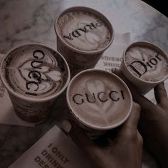 three cups of coffee with the word gucci written on them are being held by two hands