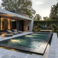 an outdoor swimming pool with lounge chairs and trees in the background at dusk or dawn