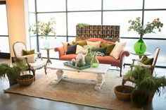 a living room filled with lots of furniture next to large window covered in plants and potted plants