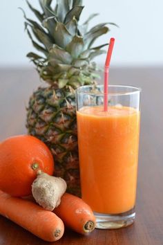 a pineapple and carrots are next to a glass of orange juice