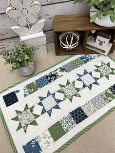 a green and white quilt on the ground next to a potted plant with flowers