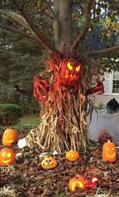 an outdoor halloween decoration with pumpkins and vines on the ground, in front of a tree