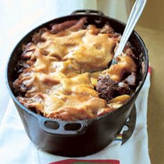 a casserole dish with meat and cheese in a black pan on a white towel