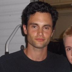 a man standing next to a woman in front of a white wall with a black shirt on