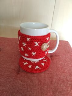 a crocheted coffee cup and saucer on a red tablecloth with white flowers