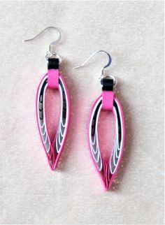 two pairs of pink and silver earrings on a white surface with one pair hanging from the ear