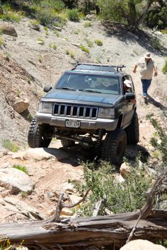 a jeep driving down a dirt road next to a man walking on the side of it