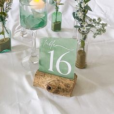 the table numbers are displayed in glass vases with greenery and candles on them