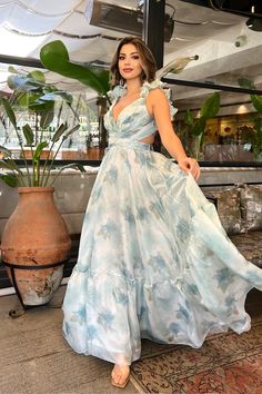 a woman in a blue and white dress standing next to a potted plant