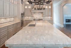 a large kitchen with marble counter tops and white cabinets, chandelier hanging from the ceiling